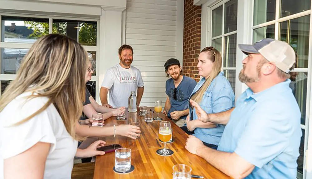 A group of people appear to be engaged in a cheerful conversation around a wooden bar table with glasses of beverages