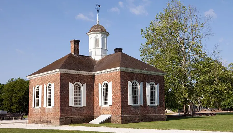 This image shows a colonial-era brick building with a white cupola, set against a clear sky with greenery surrounding it.