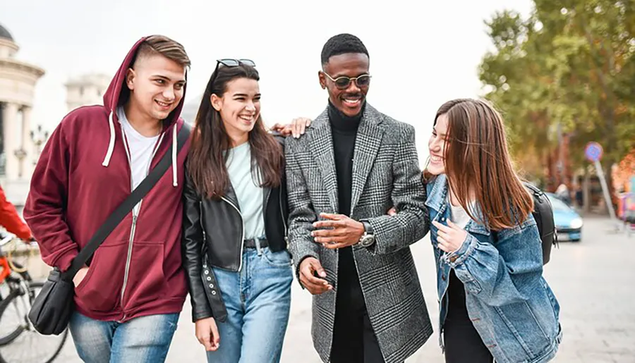 Four friends are walking and laughing together on a city street, seemingly enjoying each other's company.