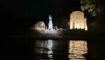 The image shows a nighttime scene with a brightly lit monument and a historic building reflecting on a body of water.