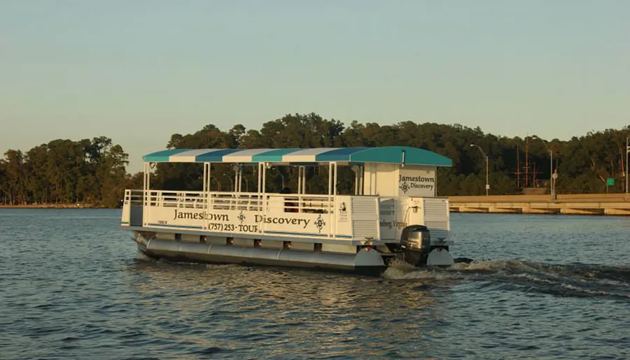A tour boat named Jamestown Discovery travels on tranquil water near a wooded shoreline.