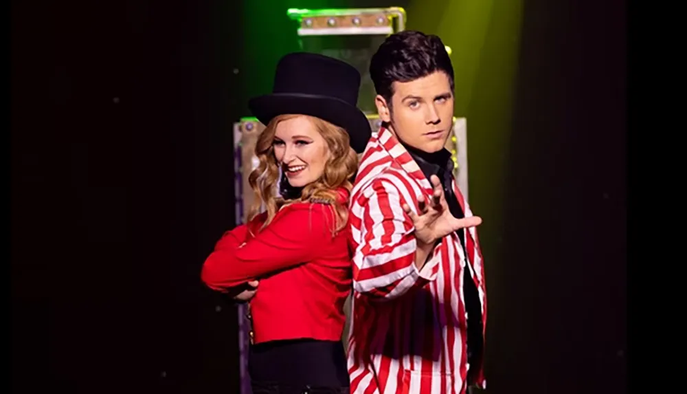 A woman in a red jacket and top hat stands back-to-back with a man in a red and white striped jacket gesturing dramatically