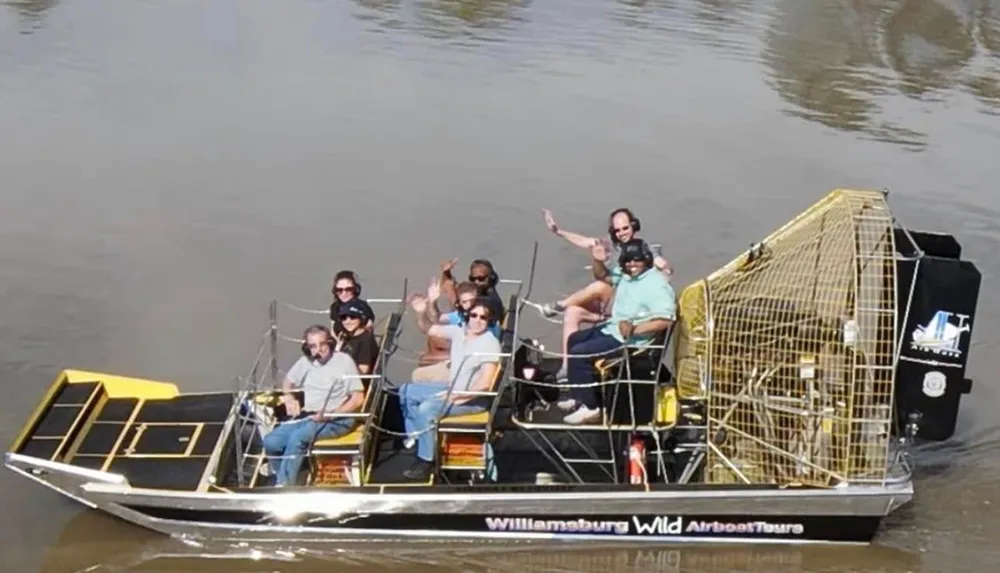 A group of people is enjoying a ride on an airboat labeled Williamsburg Wild Airboat Tours in a body of water
