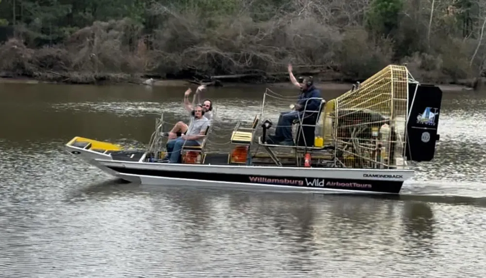 Three people are waving from an airboat cruising on a river