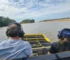 Three people wearing headphones are seated in a boat gliding on a river under a partly cloudy sky