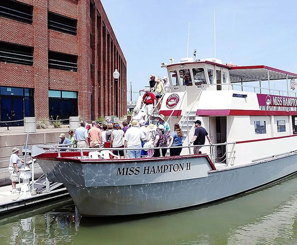 A group of passengers is boarding the Miss Hampton II tour boat on a sunny day
