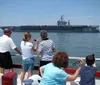 A tour boat named Miss Hampton II is cruising near a large naval aircraft carrier in a harbor