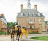 A horse-drawn carriage in historical attire is passing in front of an elegant colonial building with pedestrians nearby