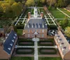 The image shows an aerial view of a large symmetrical brick mansion with a neatly landscaped garden featuring geometric patterns and pathways