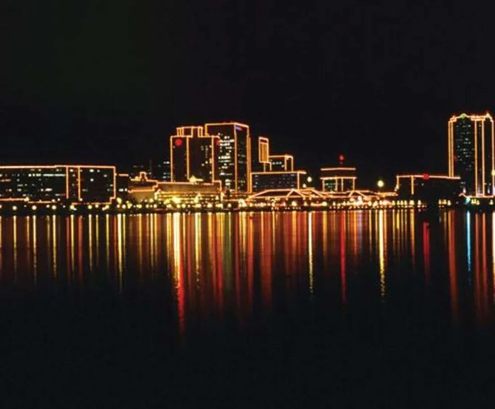 The image shows a nighttime cityscape with illuminated buildings reflected on a calm water surface