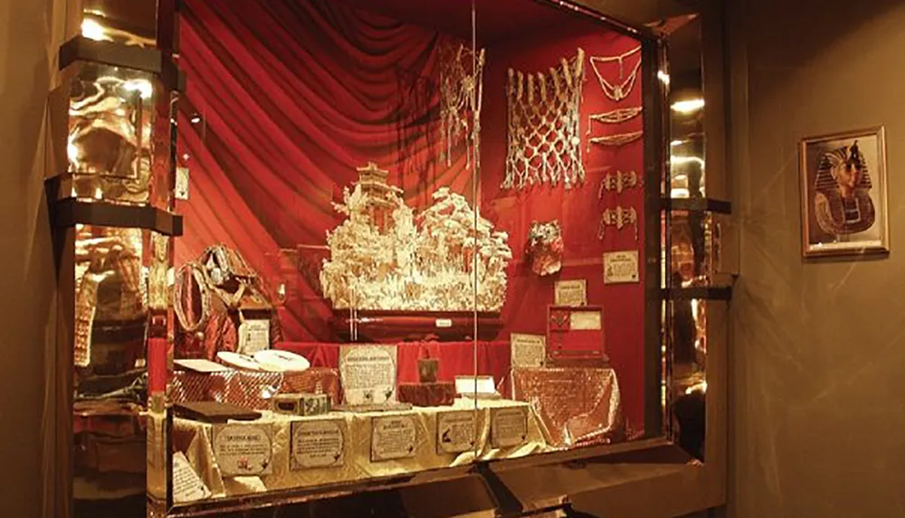 The image features a window display with a red draped background showcasing an elaborate gold collection likely to be jewelry or decorative items with an Egyptian aesthetic