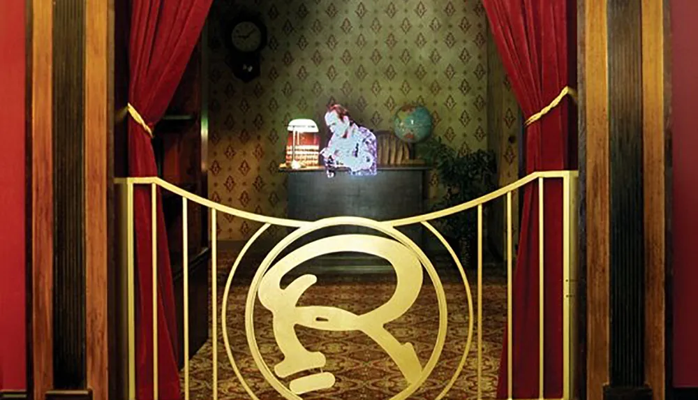 This image depicts a luxurious interior with a person behind a concierge desk ornate wallpaper red drapes and a striking gold railing with an emblem conveying a sense of grandeur or opulence