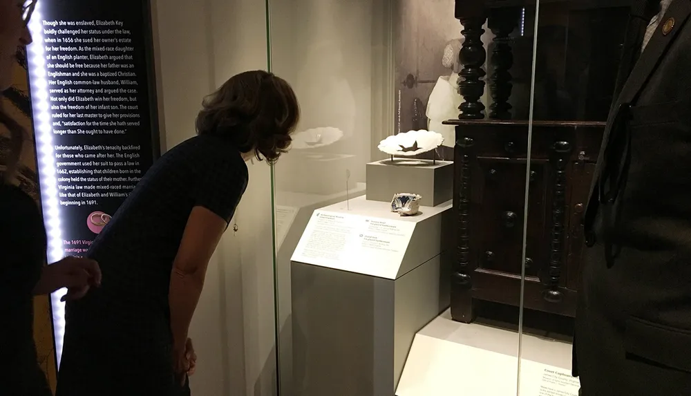 A person is observing an exhibit that includes historical artifacts and informational text in a museum display case