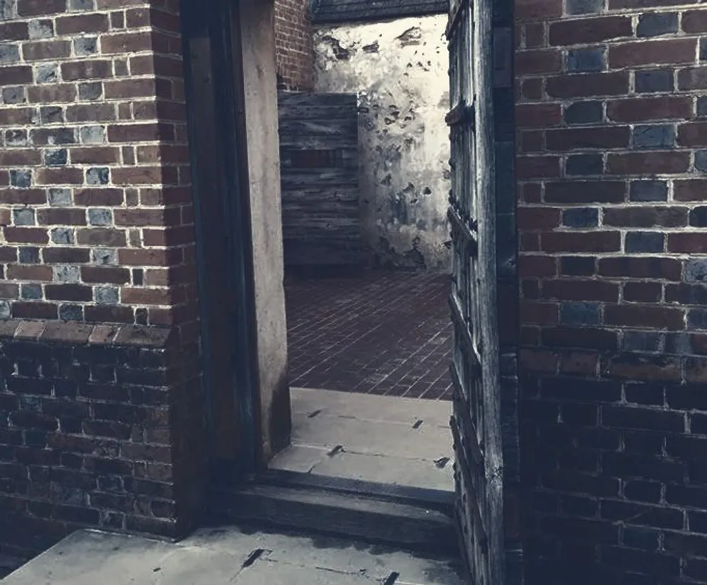 The image shows a dimly lit weathered interior with brick walls a wooden door frame and an old staircase conveying a sense of abandonment and decay