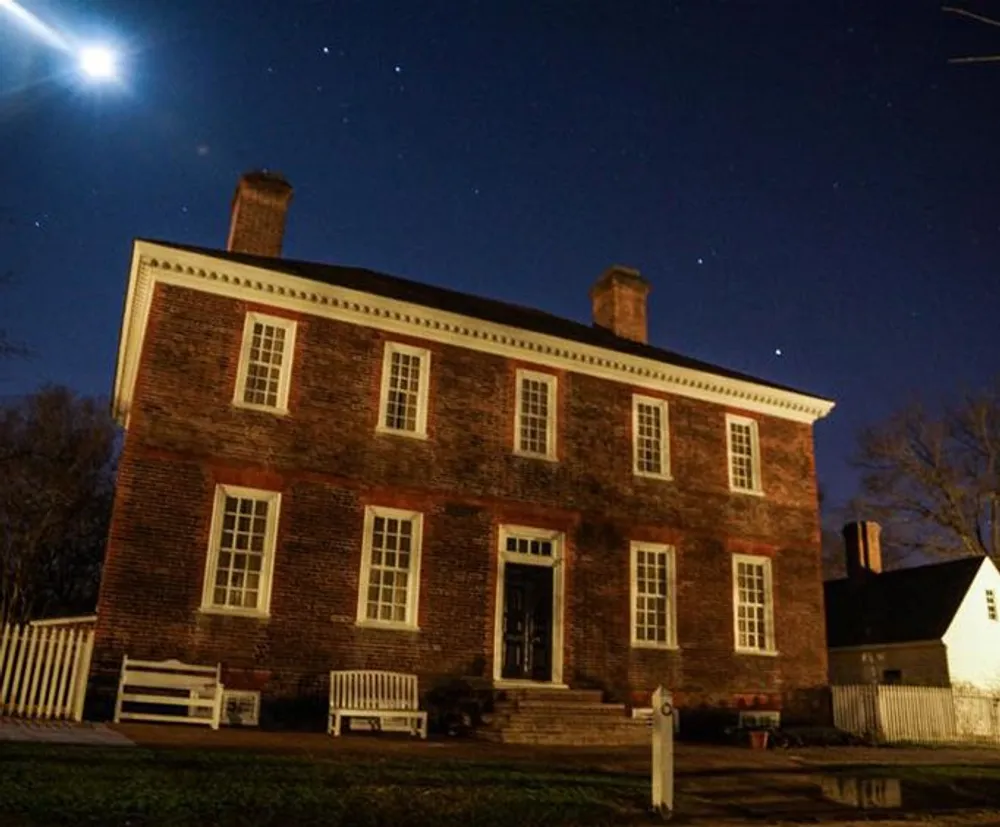 A historic brick house at night under a starry sky and a bright moon