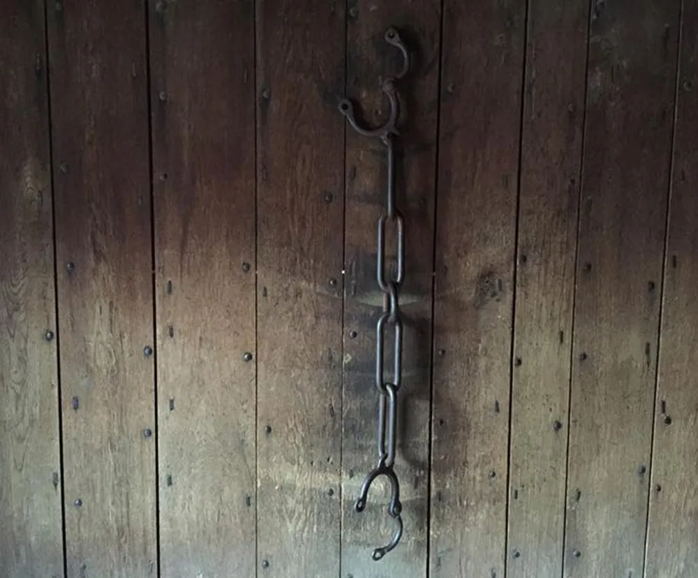 The image shows a vintage metal chain with a hook hanging against a rustic wooden door or wall with visible nail heads