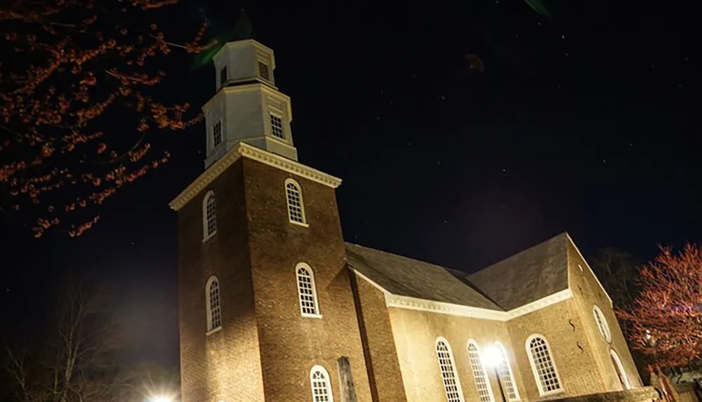 The image captures a historic-looking brick church with a steeple illuminated at night under a starry sky