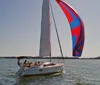 A sailboat with a colorful spinnaker sails on a sunlit body of water