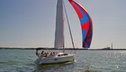 A sailboat with a colorful spinnaker sails on a sunlit body of water.