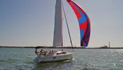 A sailboat with a colorful spinnaker sails on a sunlit body of water.