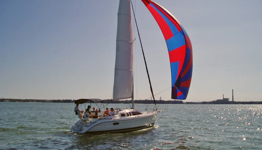 A sailboat with a colorful spinnaker sails on a sunlit body of water