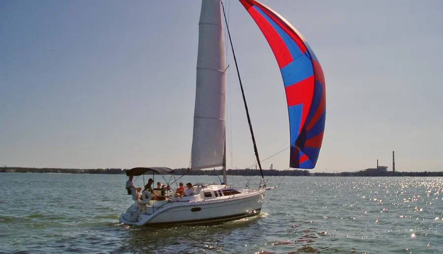 A sailboat with a colorful spinnaker sails on a sunlit body of water.