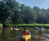 Two people are enjoying a sunny day kayaking on a calm body of water near a rustic wooden structure