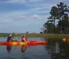 Two people are enjoying a sunny day kayaking on a calm body of water near a rustic wooden structure