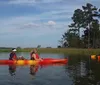 Two people are enjoying a sunny day kayaking on a calm body of water near a rustic wooden structure