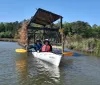 Two people are enjoying a sunny day kayaking on a calm body of water near a rustic wooden structure