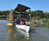 Two people are enjoying a sunny day kayaking on a calm body of water near a rustic wooden structure