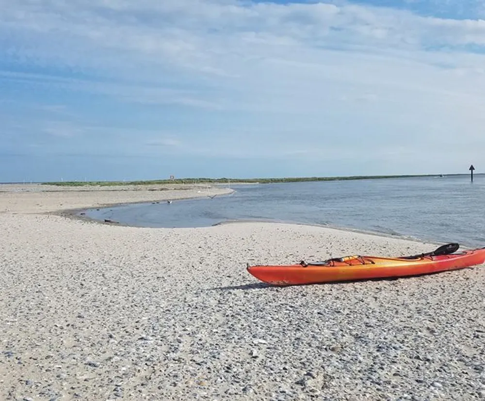 A red kayak rests on a pebbly shore by calm waters under a clear sky