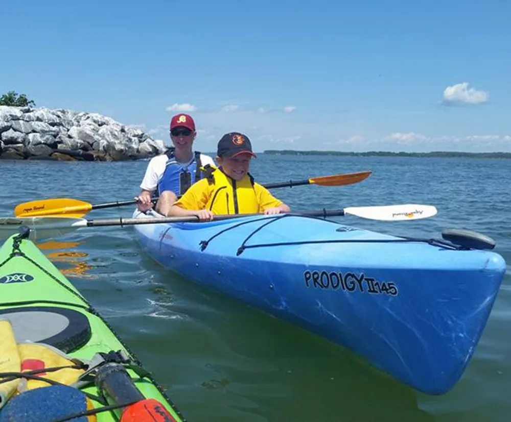 Two people in life jackets are smiling and kayaking together on a sunny day
