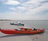 Two people in kayaks are paddling near an old lighthouse surrounded by a rocky breakwater under a clear blue sky