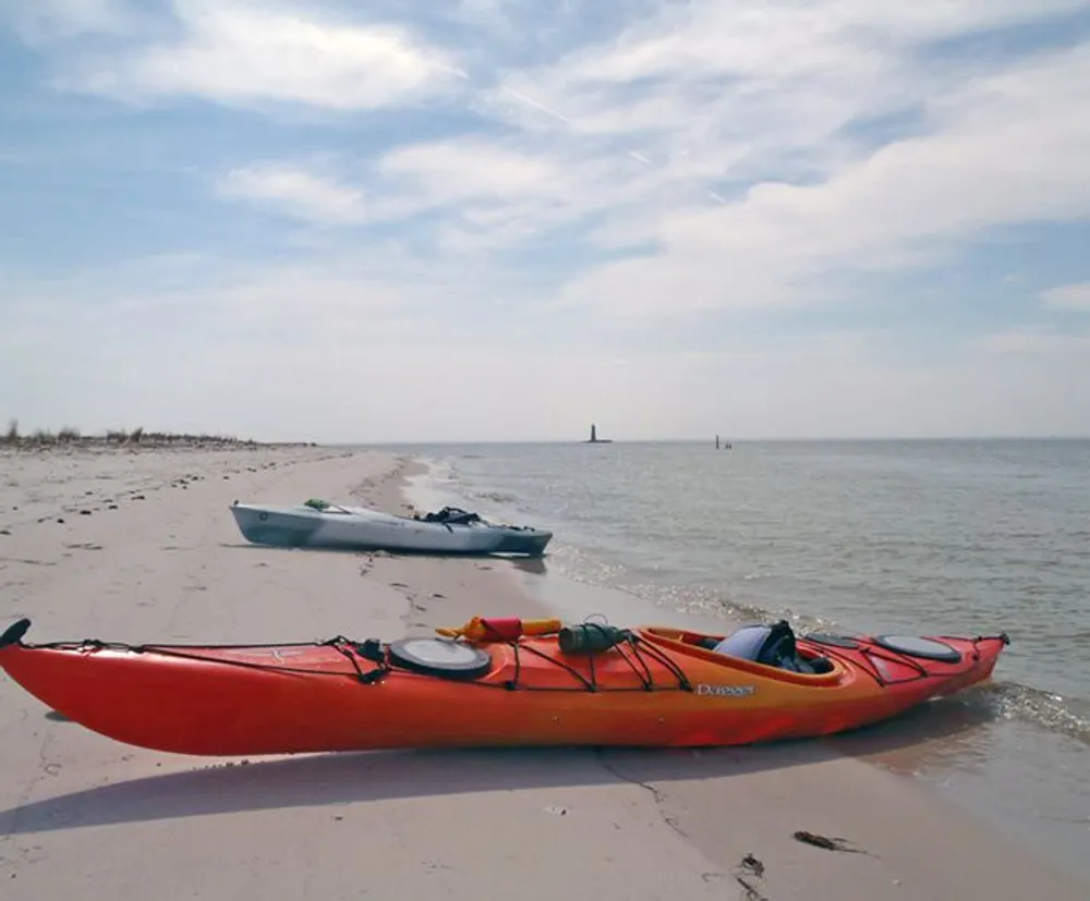 Two kayaks are resting on a sandy beach with a calm sea and blue sky in the background