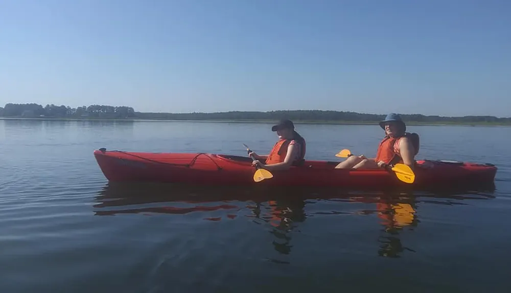 Two individuals are enjoying a calm kayaking excursion on a serene lake with clear skies