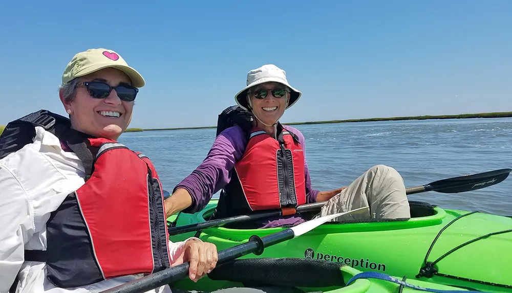 Two people are smiling while kayaking together on a sunny day