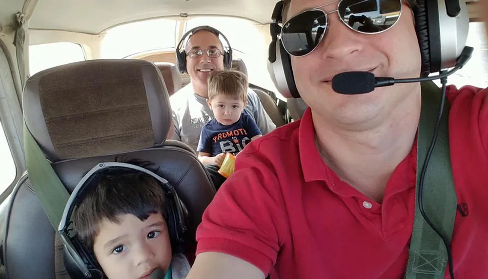 Three individuals likely a family are enjoying a flight together with headphones on as evidenced by the planes interior and their joyful expressions