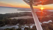 An aerial view from an airplane at sunset, showcasing a vivid sky, a reflective lake, and the silhouette of the aircraft's wing.