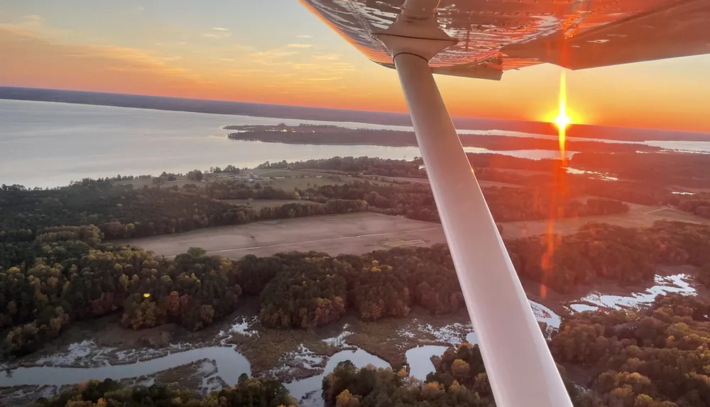 An aerial view from an airplane at sunset showcasing a vivid sky a reflective lake and the silhouette of the aircrafts wing