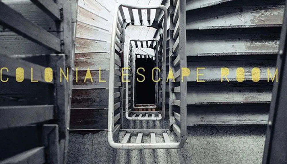 The image shows a descending spiral staircase with the phrase COLONIAL ESCAPE ROOM written in yellow across the steps suggesting an atmospheric setting for an escape room adventure