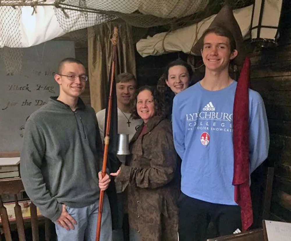A group of five individuals is smiling for the camera two of whom are holding historical or replica rifles in a room with an old maritime or pirate theme