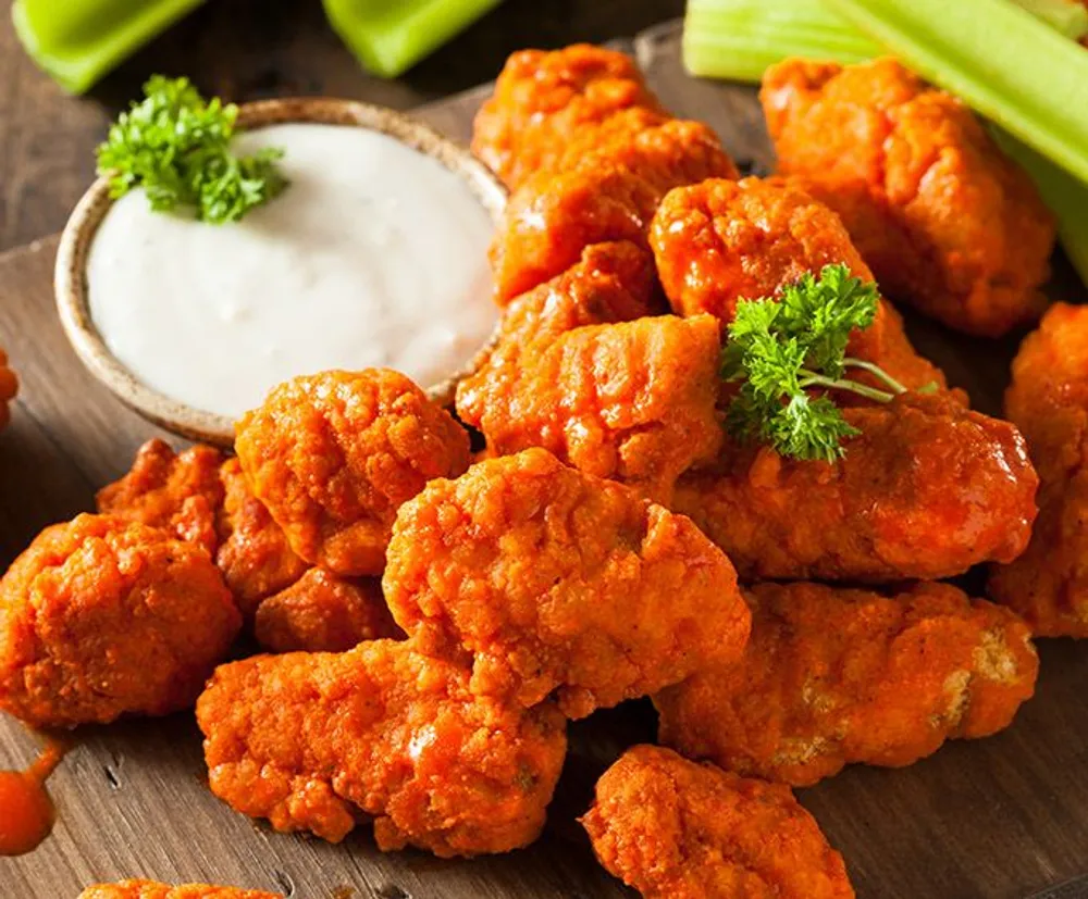 The image shows a close-up of crispy buffalo chicken wings served with celery sticks and a creamy dip typically ranch or blue cheese dressing garnished with a sprig of parsley