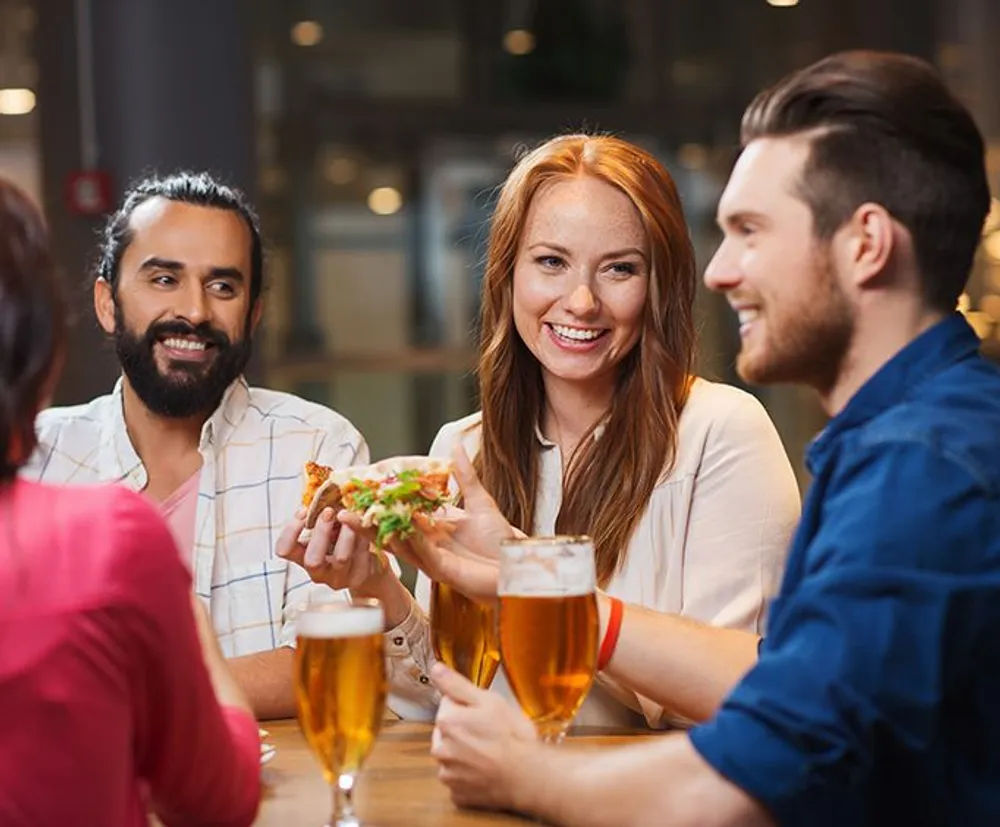 A group of friends is enjoying a lively conversation over beer and food in a casual dining setting