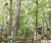 A family is interacting with a life-size dinosaur model in a forested outdoor setting