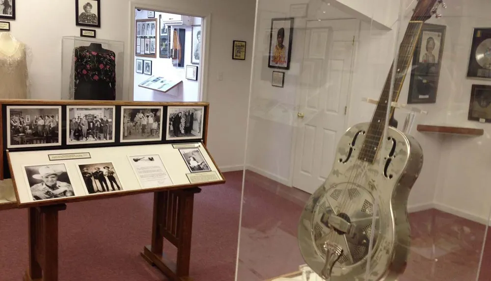 The image shows an interior view of a music-themed museum or gallery with framed photographs artifacts and a silver resonator guitar on display