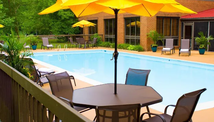 This image shows a serene poolside area with sun loungers tables under yellow umbrellas and a brick building in the background conveying a relaxing outdoor setting