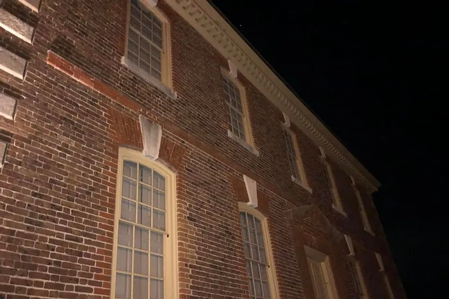 The image shows the facade of a brick building at night, illuminated from below, highlighting its windows and architectural details.