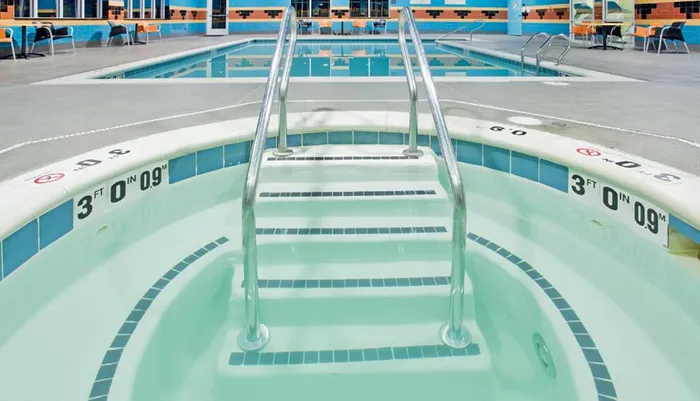 A symmetrical view of stainless steel pool steps leading down into a shallow section of a pool with clear blue water marked with depth indicators