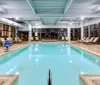 The image shows an indoor swimming pool area with lounge chairs and facilities typically found in a hotel or recreational center